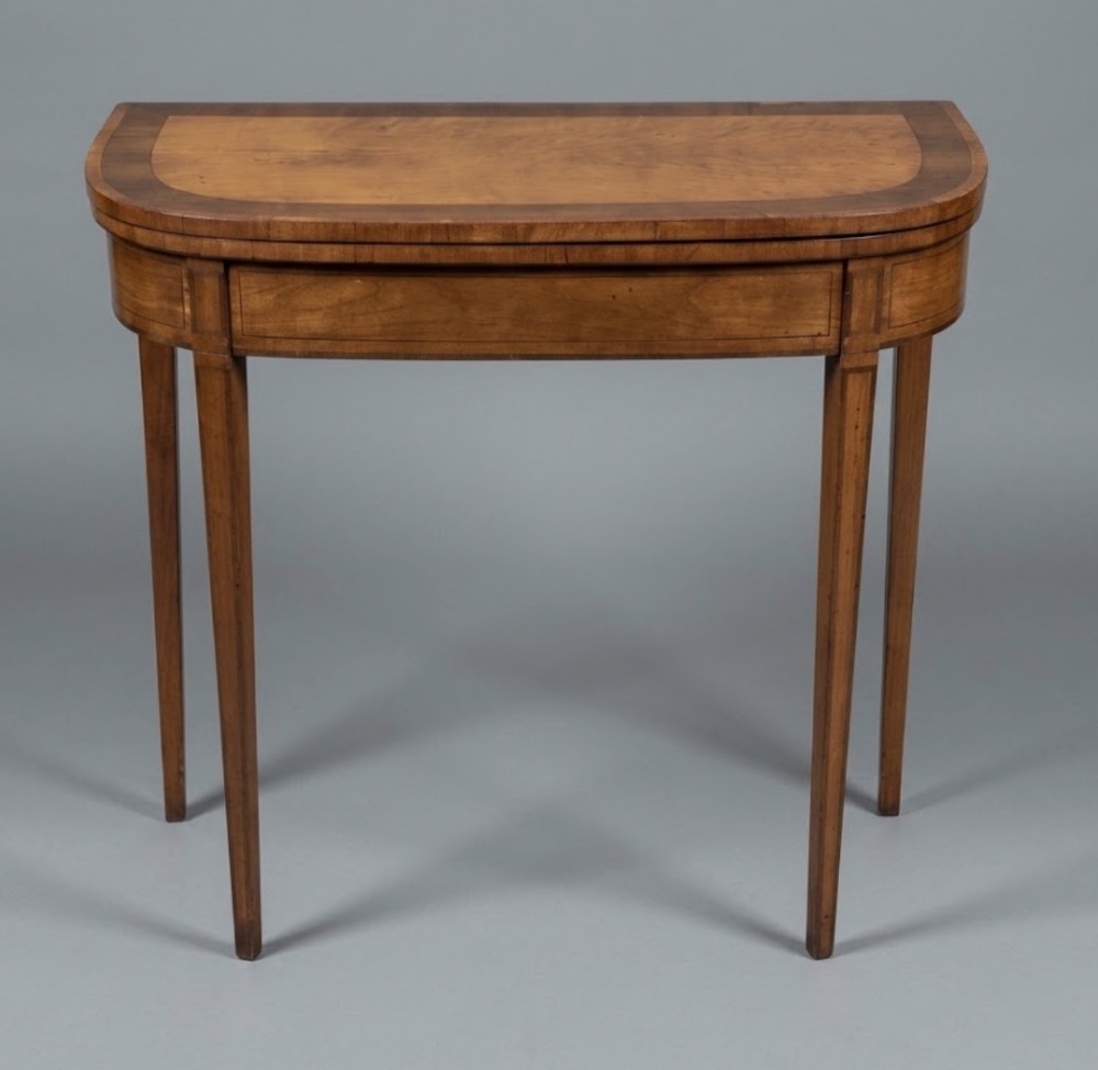 A George III D-shaped satinwood card table featuring rosewood crossbanding, a folding top, and four square tapered legs.