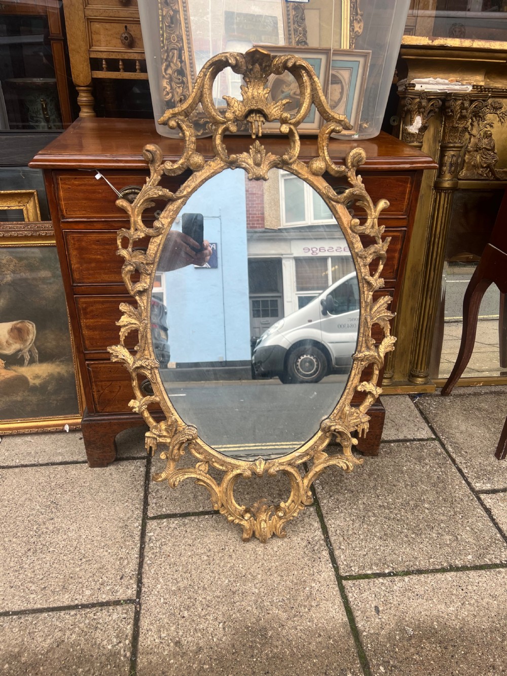 An 18th-century style oval wall mirror featuring a carved giltwood frame with openwork scrollwork and acanthus leaf cresting. View XII