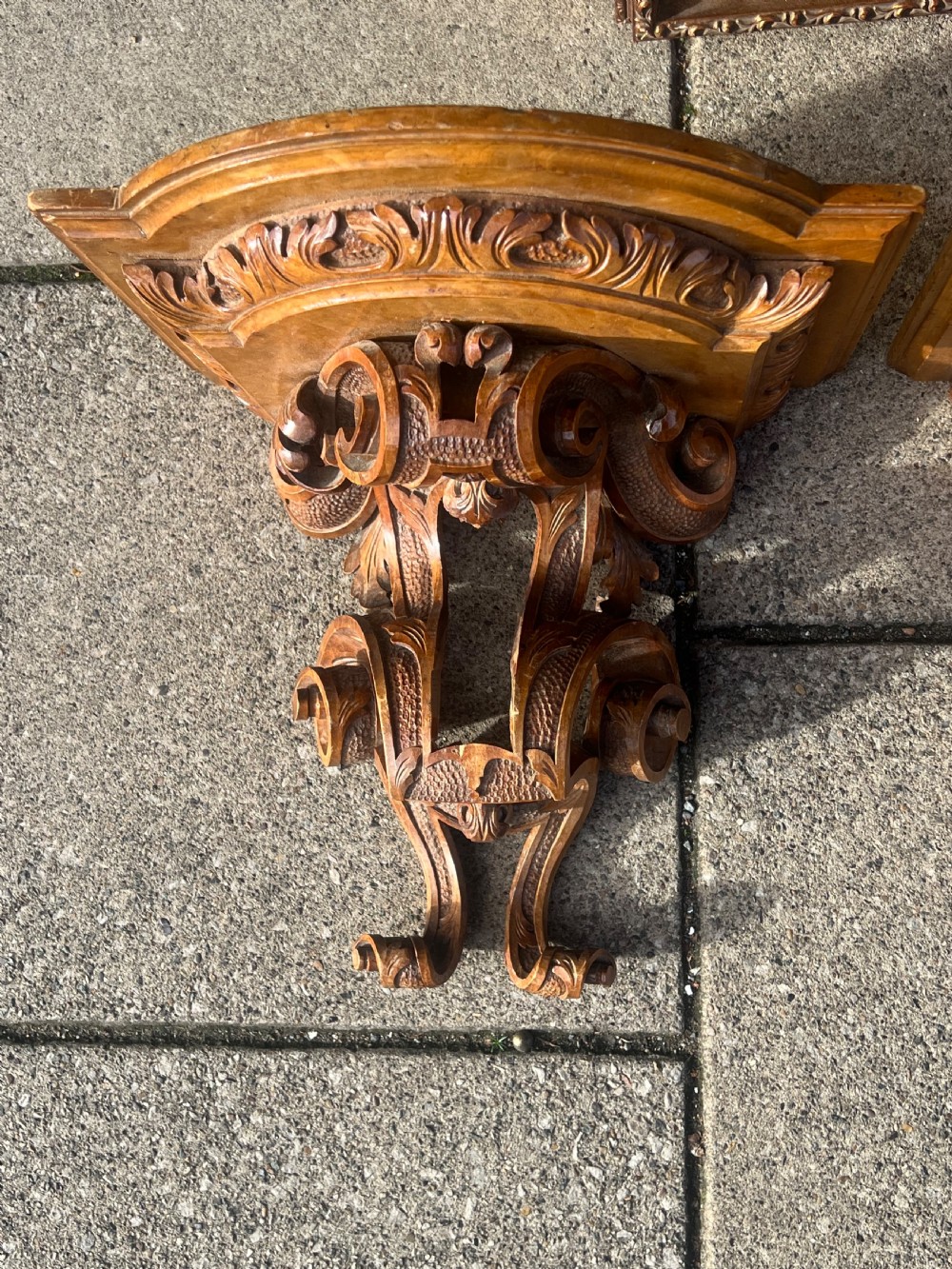 A pair of Georgian carved walnut wall brackets featuring scrollwork and acanthus leaf details mounted against a plain wall. View VI