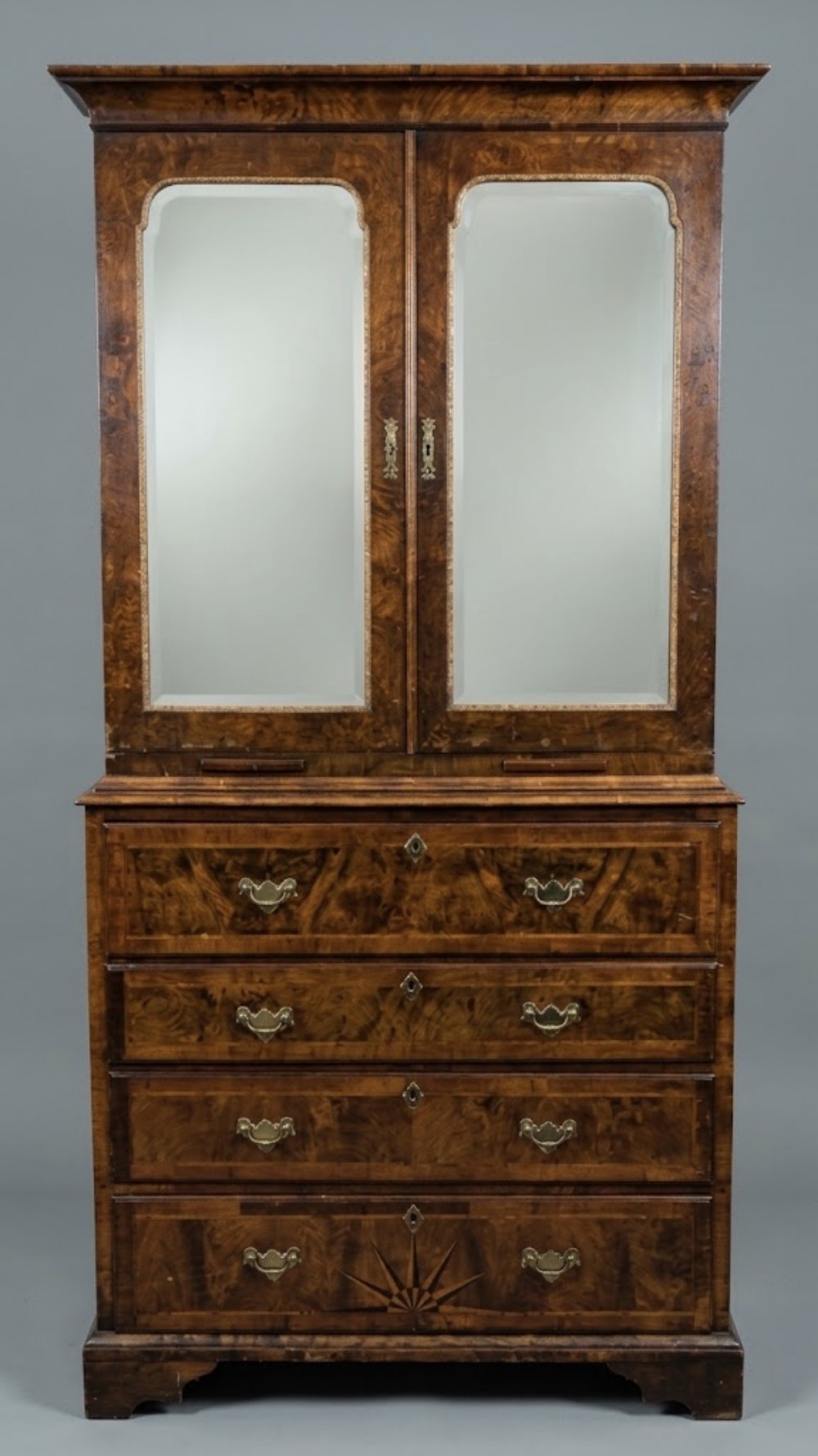 An eighteenth-century walnut secretaire bookcase featuring a mirrored two-door upper section above four drawers with brass drop handles and a starburst inlay.