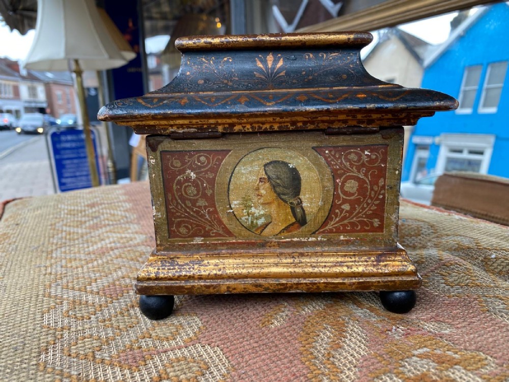 A small rectangular wooden casket featuring a painted medieval figure scene on the front, a gilded stepped lid, and black ball feet. View III
