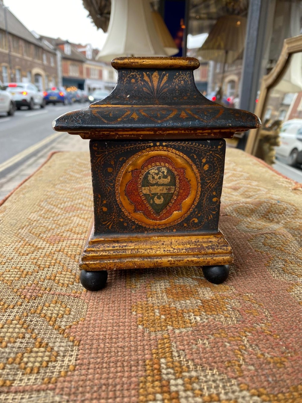 A small rectangular wooden casket featuring a painted medieval figure scene on the front, a gilded stepped lid, and black ball feet. View IV