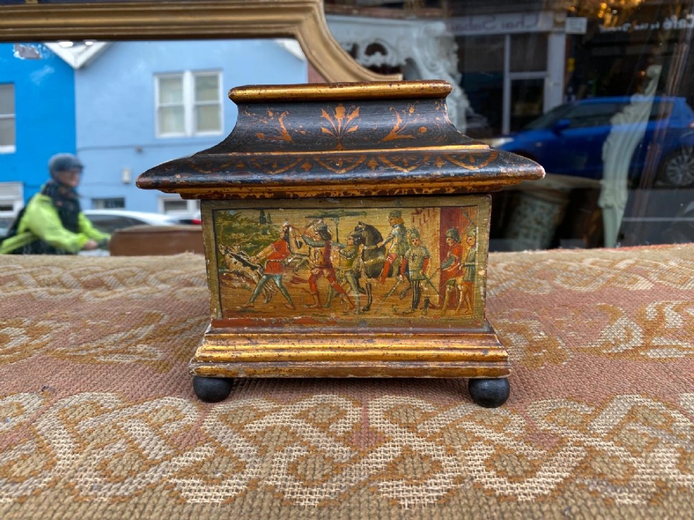 A small rectangular wooden casket featuring a painted medieval figure scene on the front, a gilded stepped lid, and black ball feet. View VII