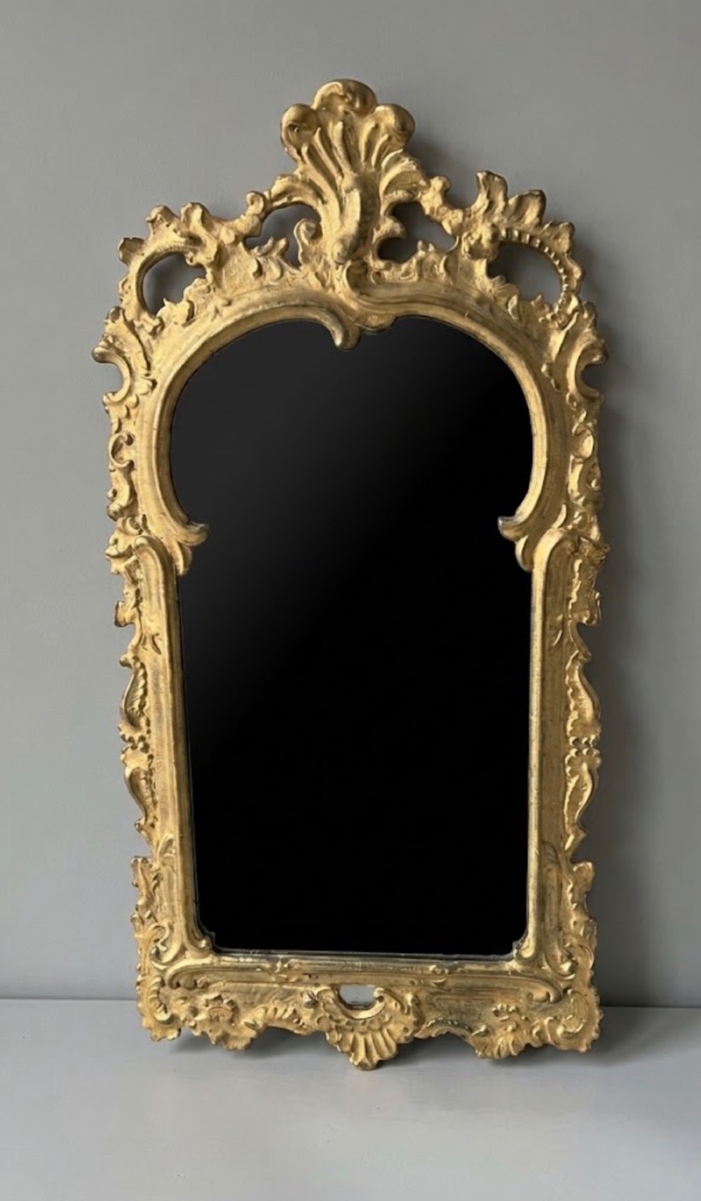 An 18th-century style wall mirror featuring an ornate carved gold giltwood frame with pierced cresting and acanthus leaf detail surrounding a shaped glass pane.