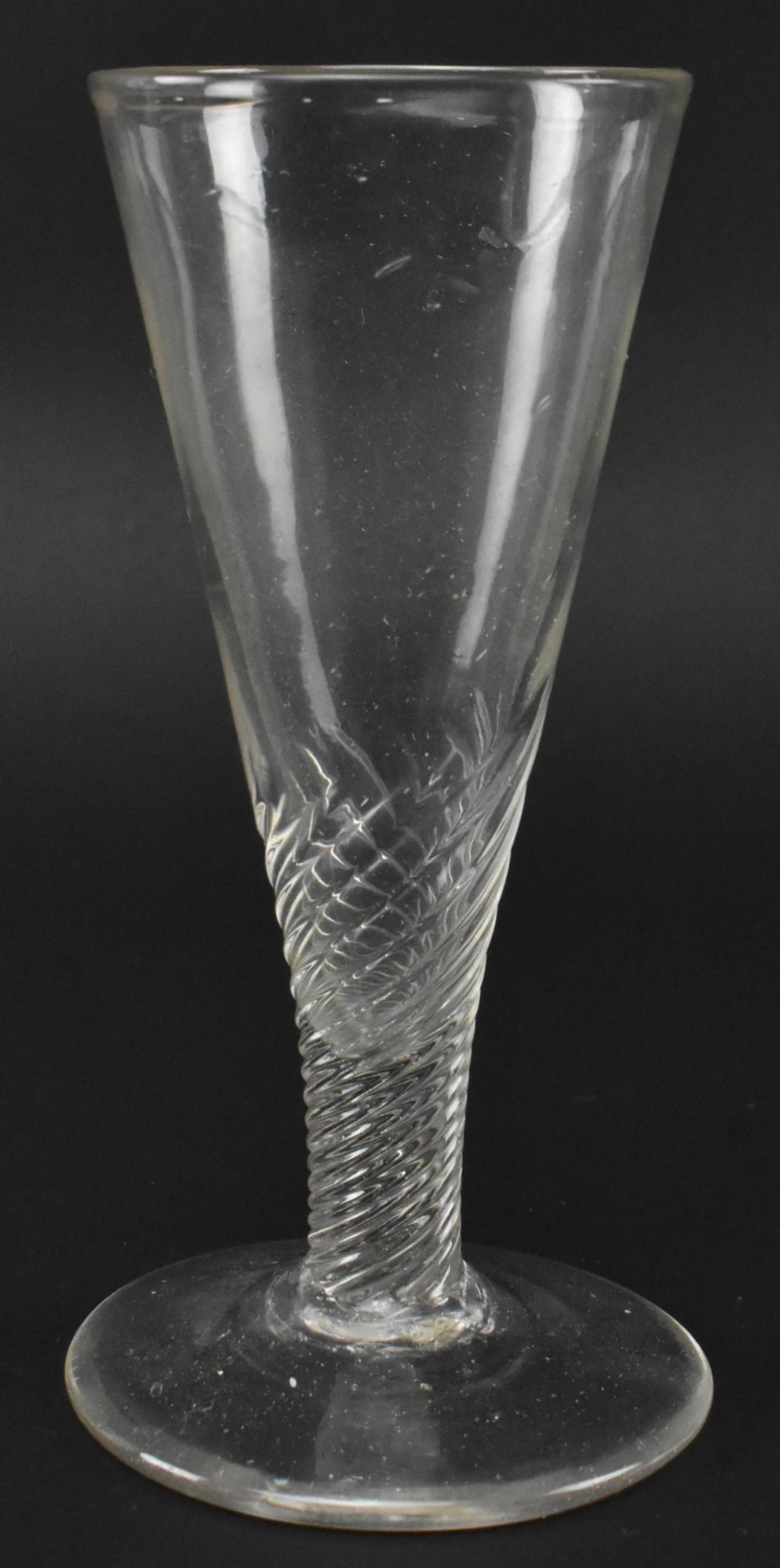 A Georgian clear hand-blown glass ale flute featuring half-wrythen spiral fluting on the lower bowl above a conical foot.