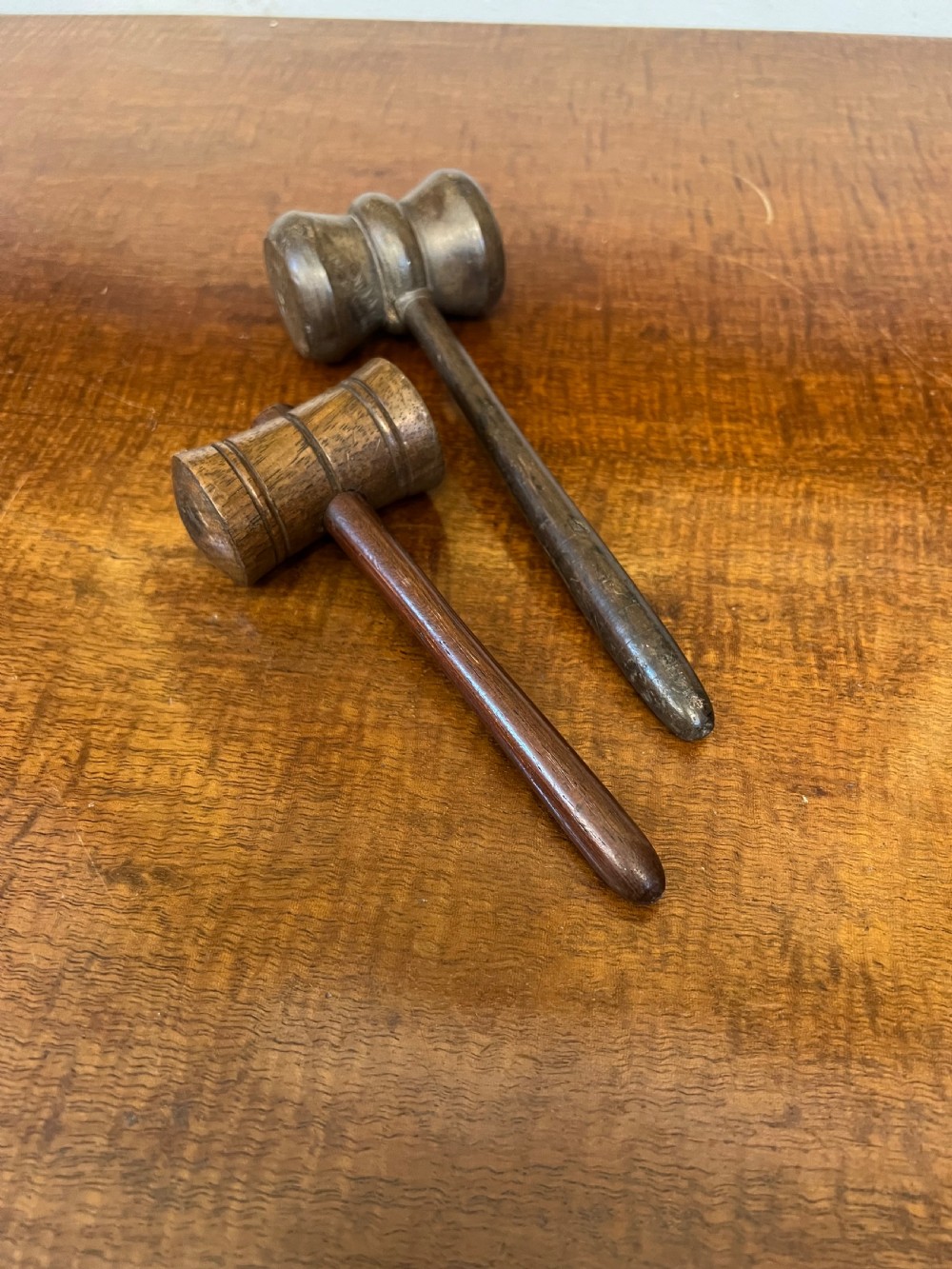 Pair of turned wooden gavels with cylindrical heads and slender tapered handles resting on a wooden surface.