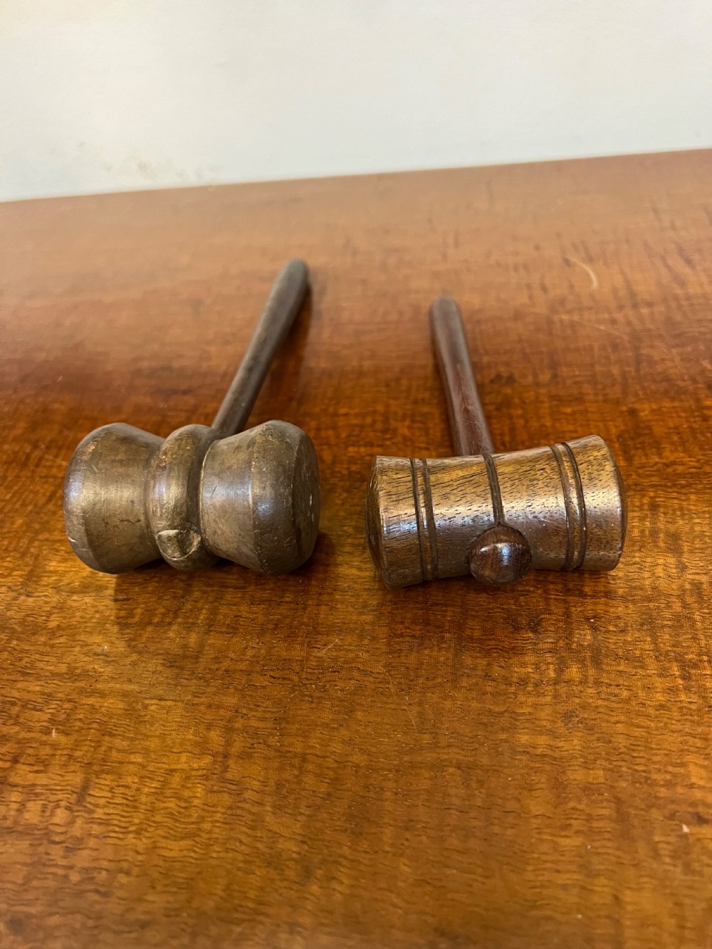 Pair of turned wooden gavels with cylindrical heads and slender tapered handles resting on a wooden surface. View II