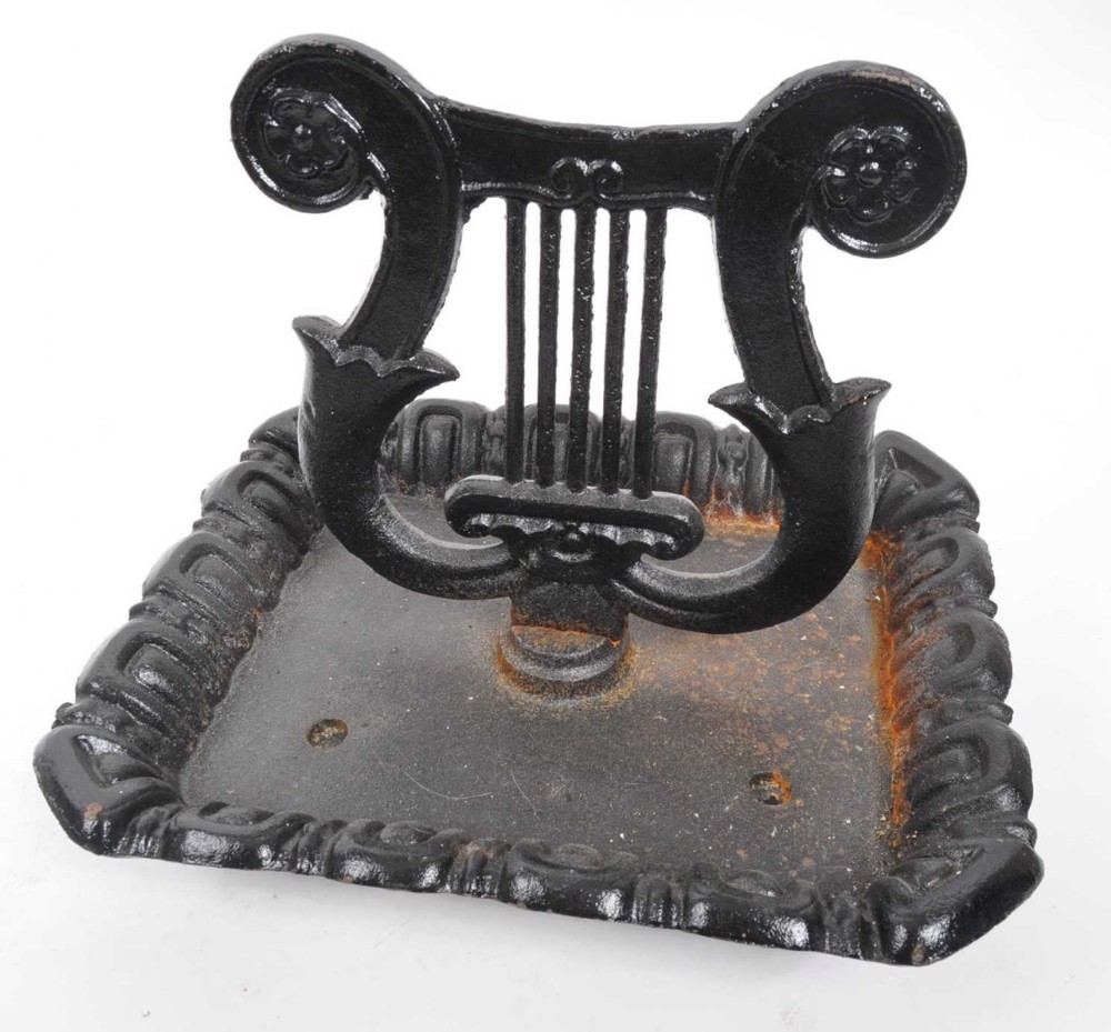 A black nineteenth-century cast iron boot scraper with a lyre motif mounted on a square tray base with molded edging.