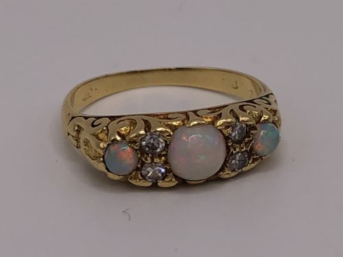 fig 1. An antique yellow gold ring featuring three oval opal cabochons flanked by small accent diamonds within a carved scrollwork gallery.