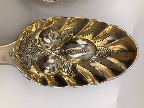 fig 1. A pair of sterling silver serving spoons featuring gilded bowls with raised fruit motifs and elaborately chased handles ending in shell designs.