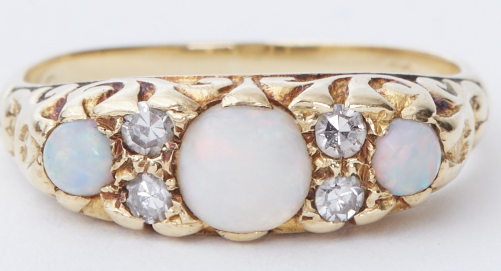 An antique yellow gold ring featuring three oval opal cabochons flanked by small accent diamonds within a carved scrollwork gallery.