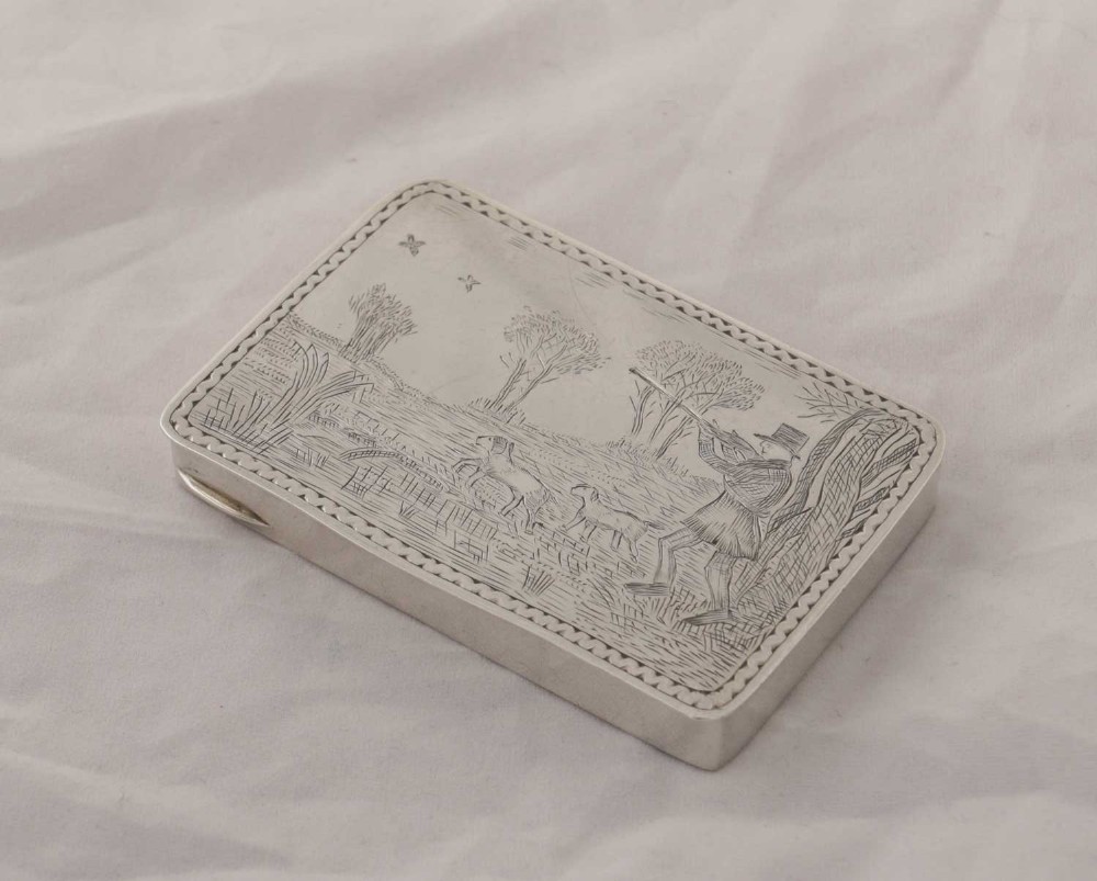 An oblong silver box featuring a detailed pictorial engraving of a hunter aiming at flying birds with gundogs in a field.