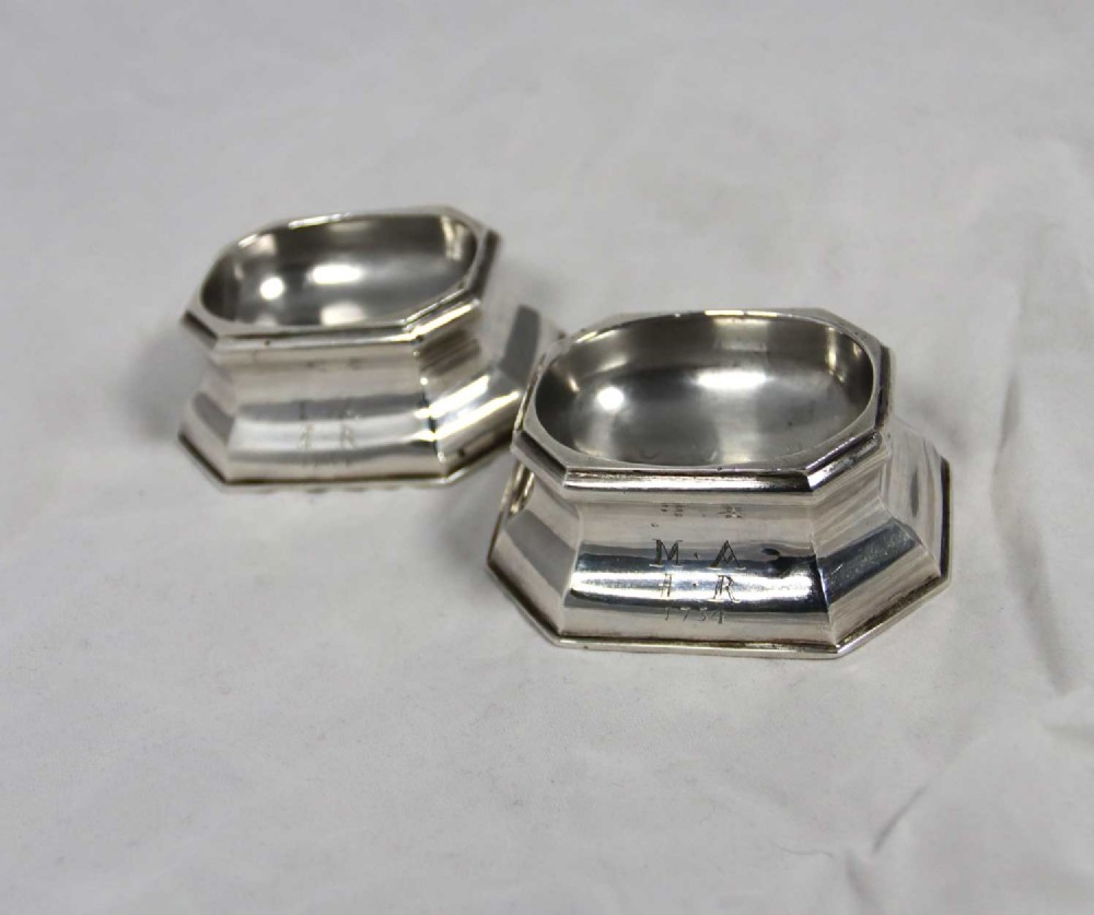 A pair of small octagonal George II sterling silver trencher salts featuring central oval depressions and engraved inscriptions on their stepped bases.