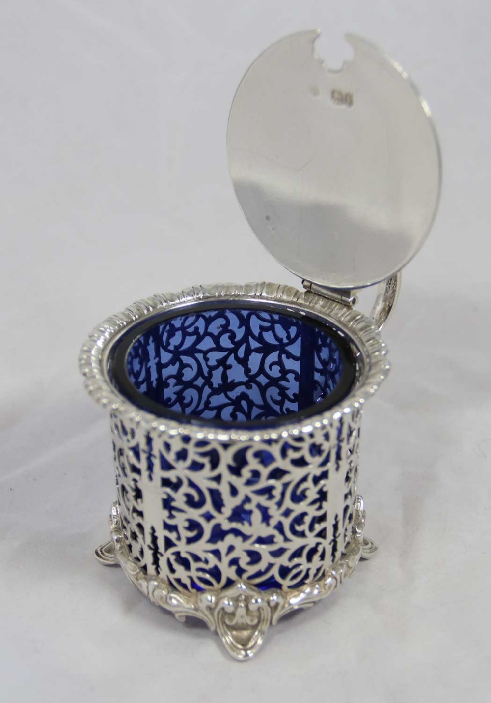 A Victorian silver mustard pot featuring openwork scroll fretwork, a hinged lid, and a cobalt blue glass liner.