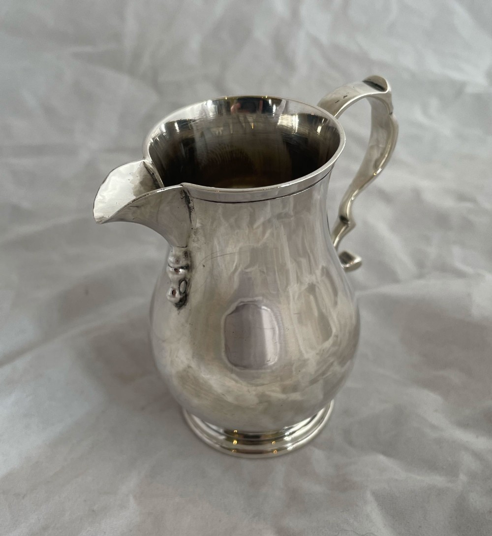 A sterling silver cream jug featuring a baluster shape, a sparrow beak spout, a curved scroll handle, and a circular moulded base.