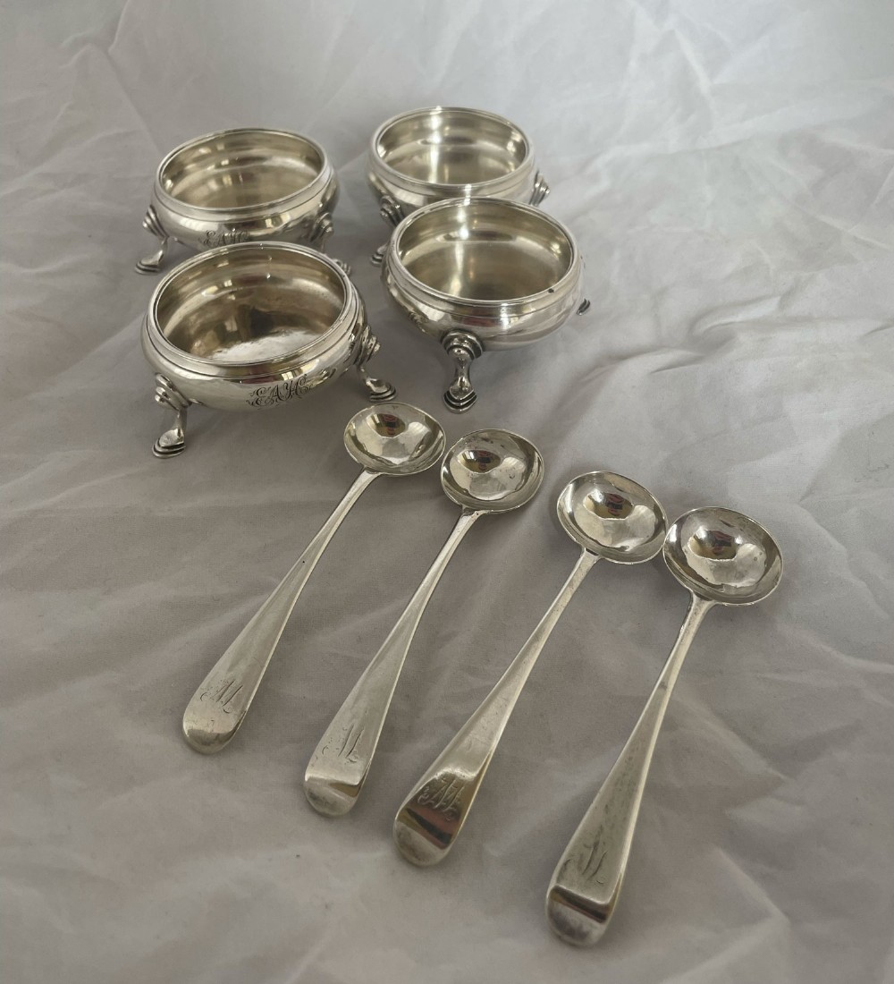 A set of four circular sterling silver salt cellars with tripod legs and four matching silver spoons.