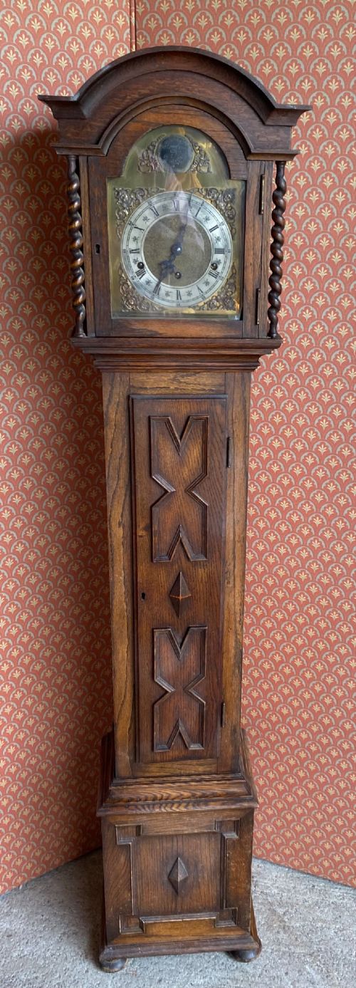 A Jacobean style oak grandmother clock featuring an arched top, barley twist columns, and a carved geometric panel door. View V