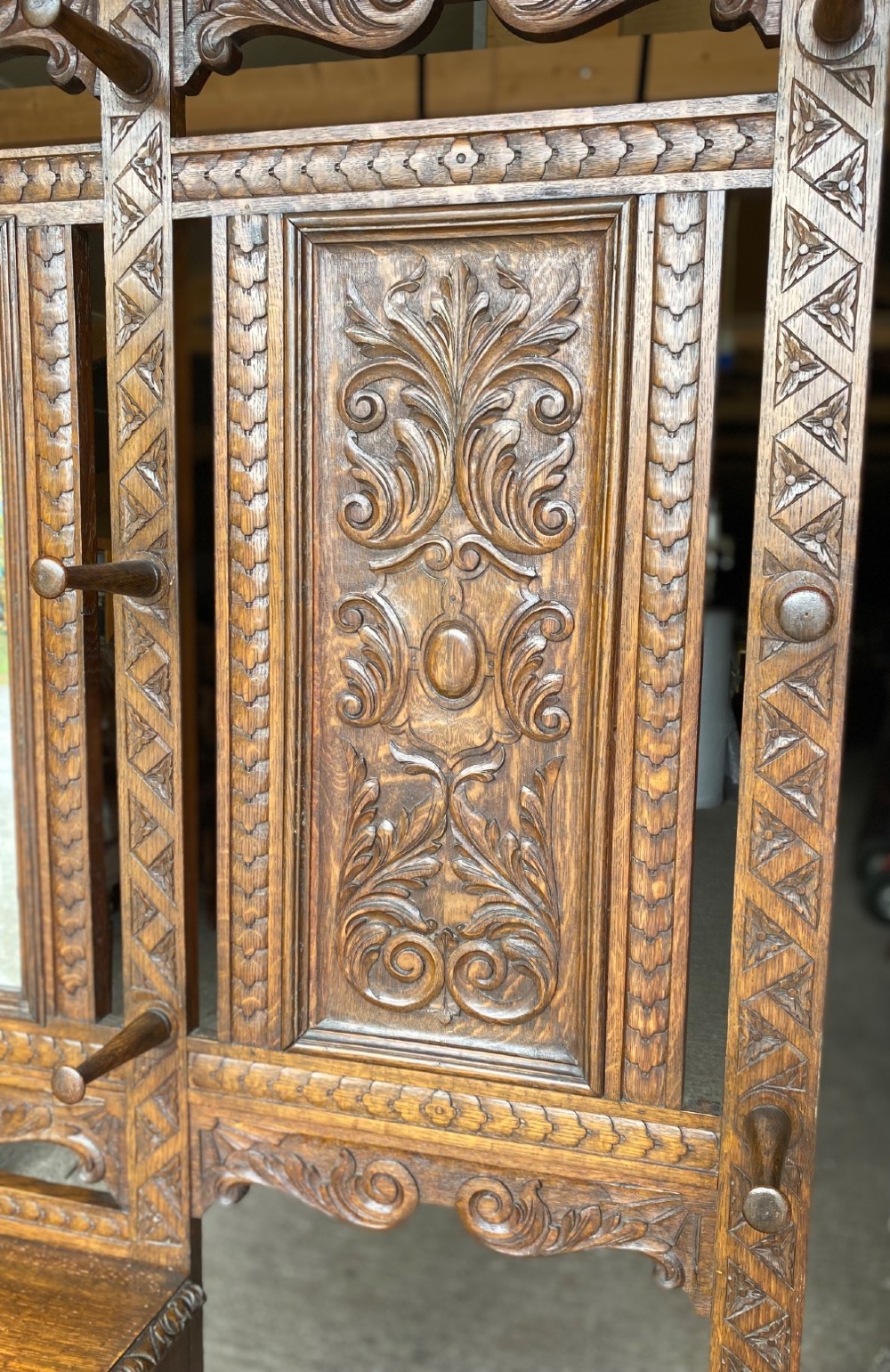 A tall carved oak hall stand featuring a central mirror, coat pegs, carved decorative panels, a small table section, and an umbrella holder with a drip tray. View IX