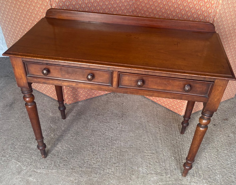 A Victorian mahogany writing table featuring a low gallery upstand, two drawer fronts with turned wooden knobs, and four turned legs.