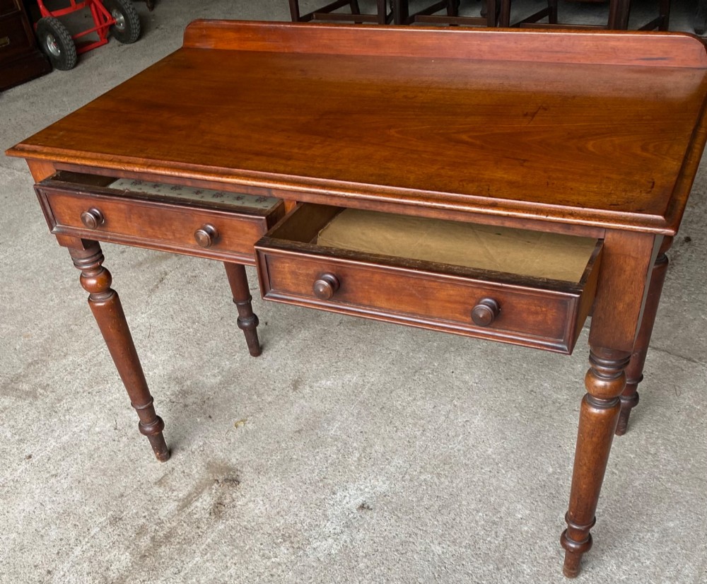 A Victorian mahogany writing table featuring a low gallery upstand, two drawer fronts with turned wooden knobs, and four turned legs. View IV