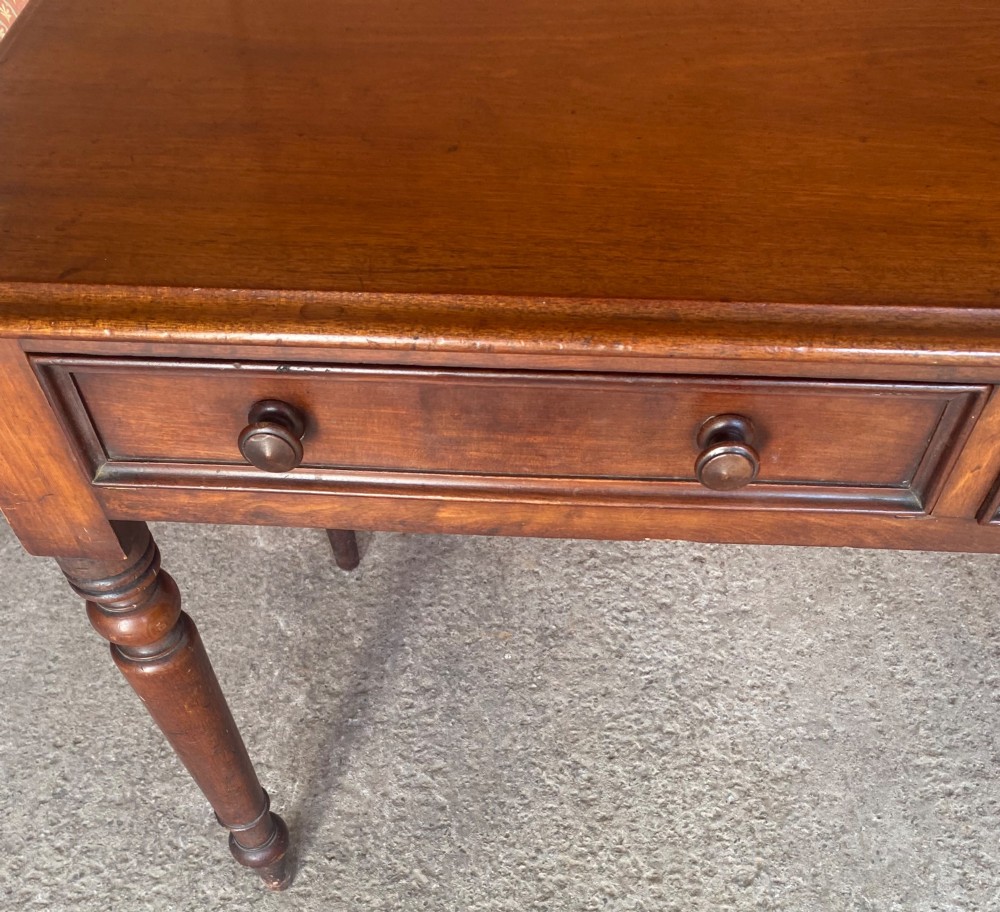 A Victorian mahogany writing table featuring a low gallery upstand, two drawer fronts with turned wooden knobs, and four turned legs. View V