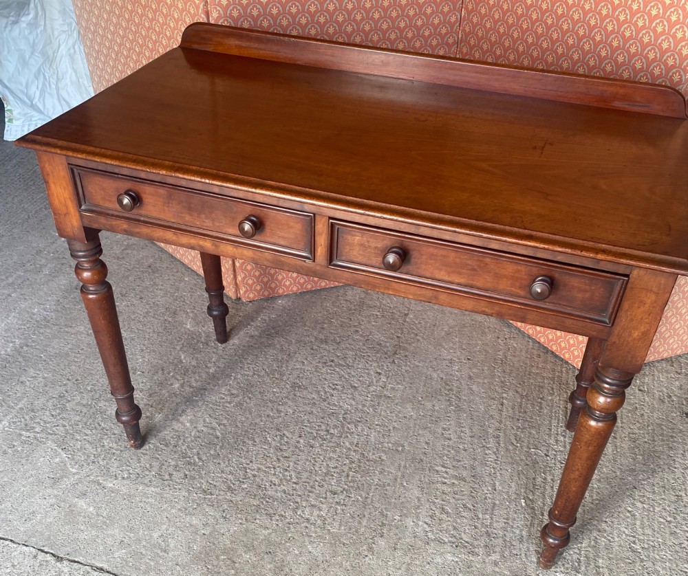 A Victorian mahogany writing table featuring a low gallery upstand, two drawer fronts with turned wooden knobs, and four turned legs. View VI