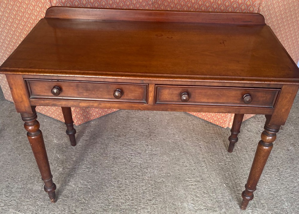 A Victorian mahogany writing table featuring a low gallery upstand, two drawer fronts with turned wooden knobs, and four turned legs. View VII