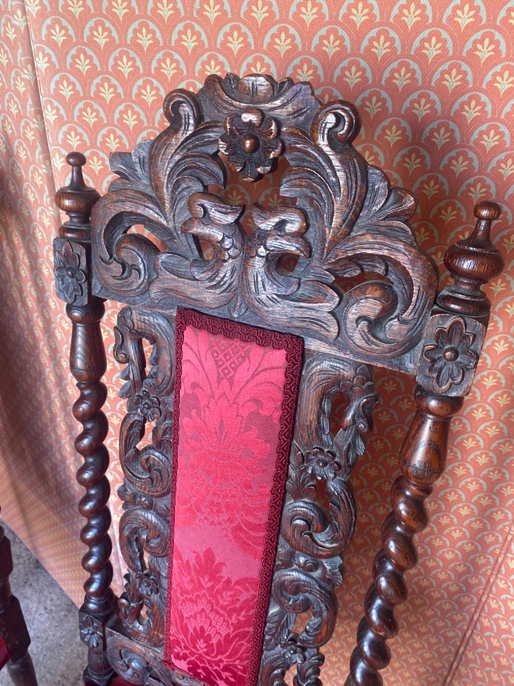 A pair of high-backed carved oak hall chairs featuring elaborate scrollwork, barley twist pillars, and red pattern damask upholstery. View V