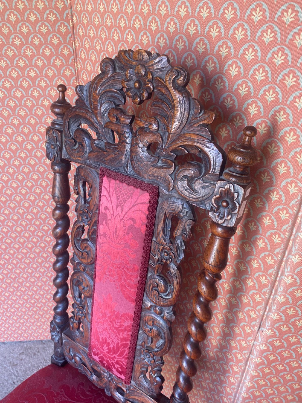 A pair of high-backed carved oak hall chairs featuring elaborate scrollwork, barley twist pillars, and red pattern damask upholstery. View VI
