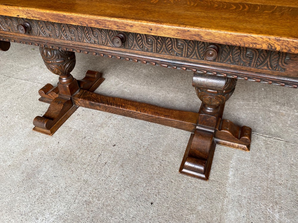 A rectangular solid oak refectory dining table featuring a carved frieze, carved bulbous turned legs, and a low stretcher base. View III