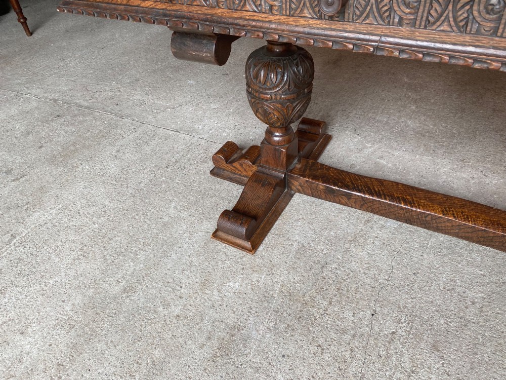 A rectangular solid oak refectory dining table featuring a carved frieze, carved bulbous turned legs, and a low stretcher base. View VII