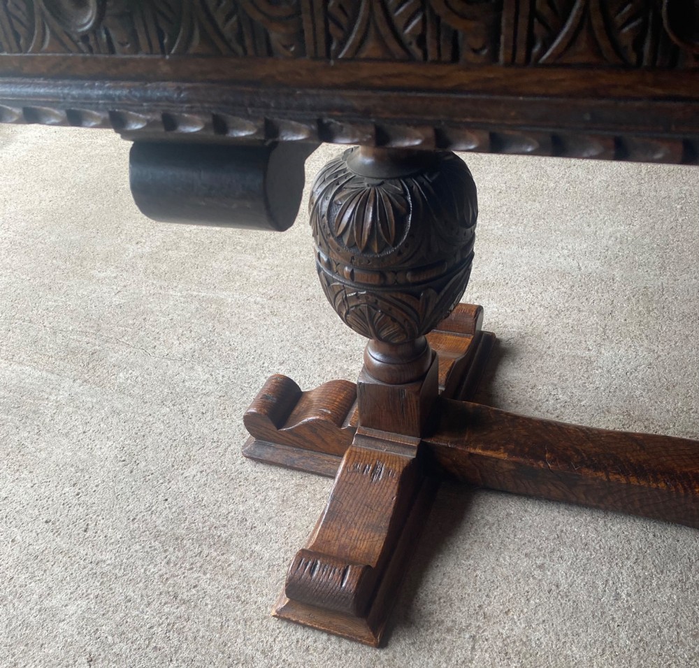 A rectangular solid oak refectory dining table featuring a carved frieze, carved bulbous turned legs, and a low stretcher base. View X