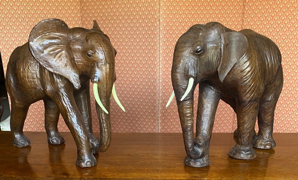A pair of hand-crafted dark brown leather elephant statues standing with raised trunks and light-coloured tusks.