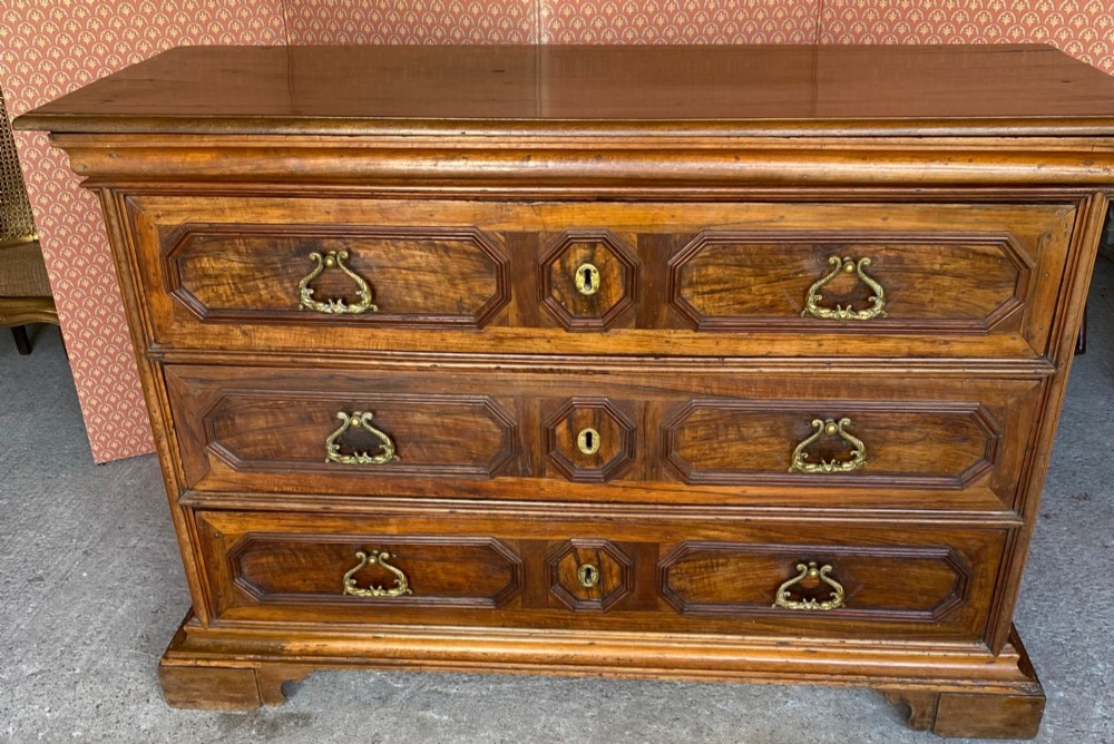 An 18th-century Italian walnut chest of drawers featuring geometric panel mouldings, brass drop handles, and bracket feet.