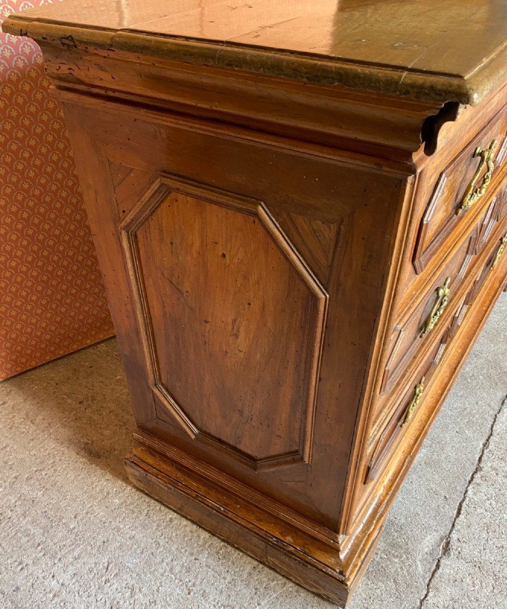 An 18th-century Italian walnut chest of drawers featuring geometric panel mouldings, brass drop handles, and bracket feet. View V