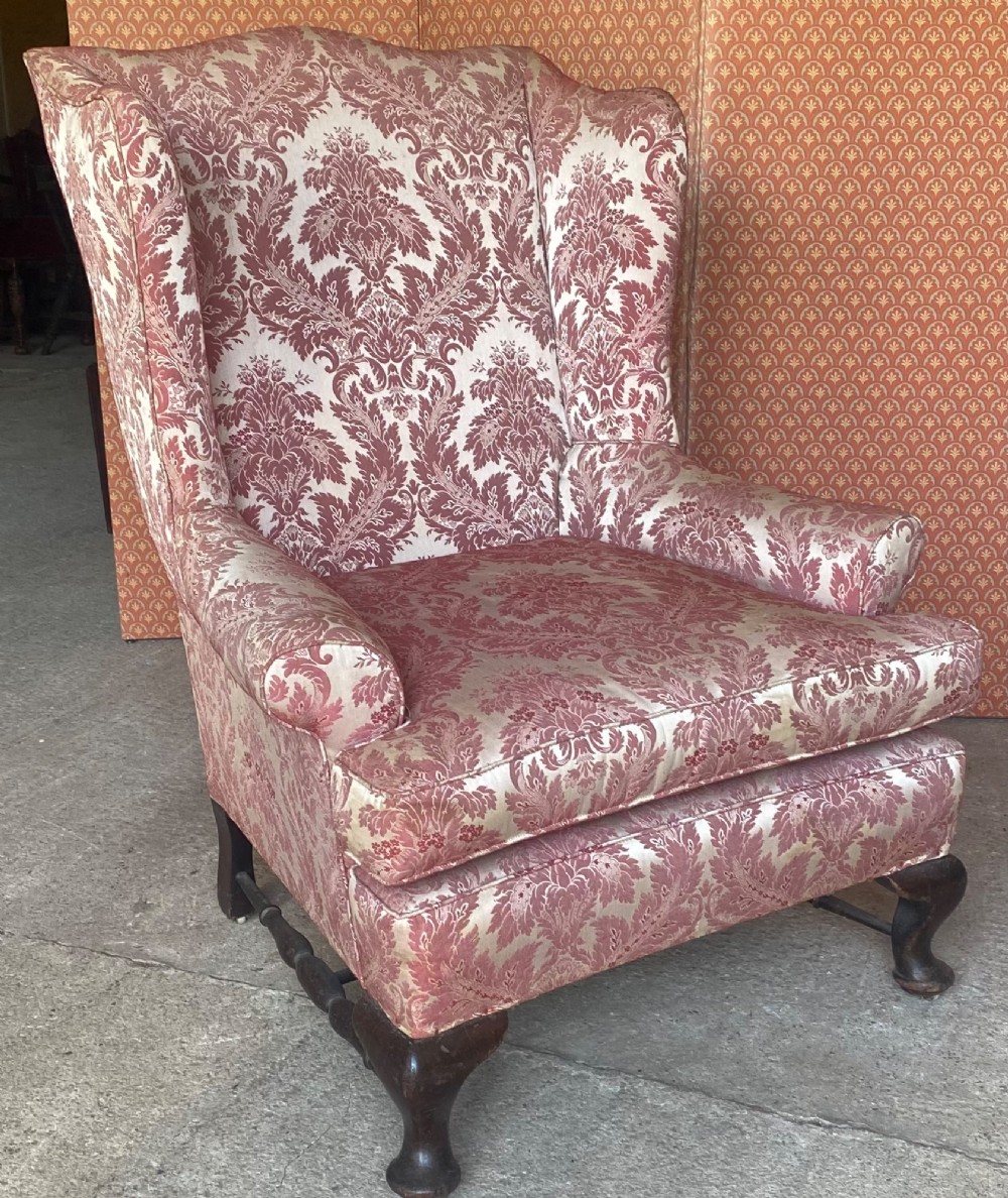A high-back wingback armchair upholstered in rose pink and cream damask fabric, featuring rolled arms, a fitted seat cushion, and dark carved wooden legs.