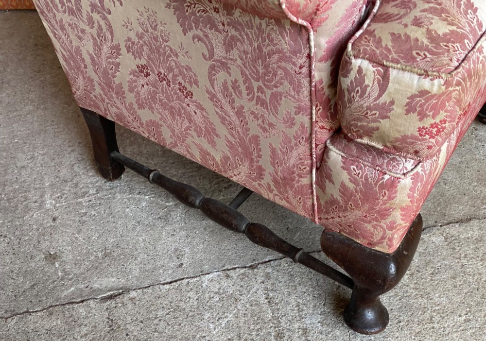 A high-back wingback armchair upholstered in rose pink and cream damask fabric, featuring rolled arms, a fitted seat cushion, and dark carved wooden legs. View II