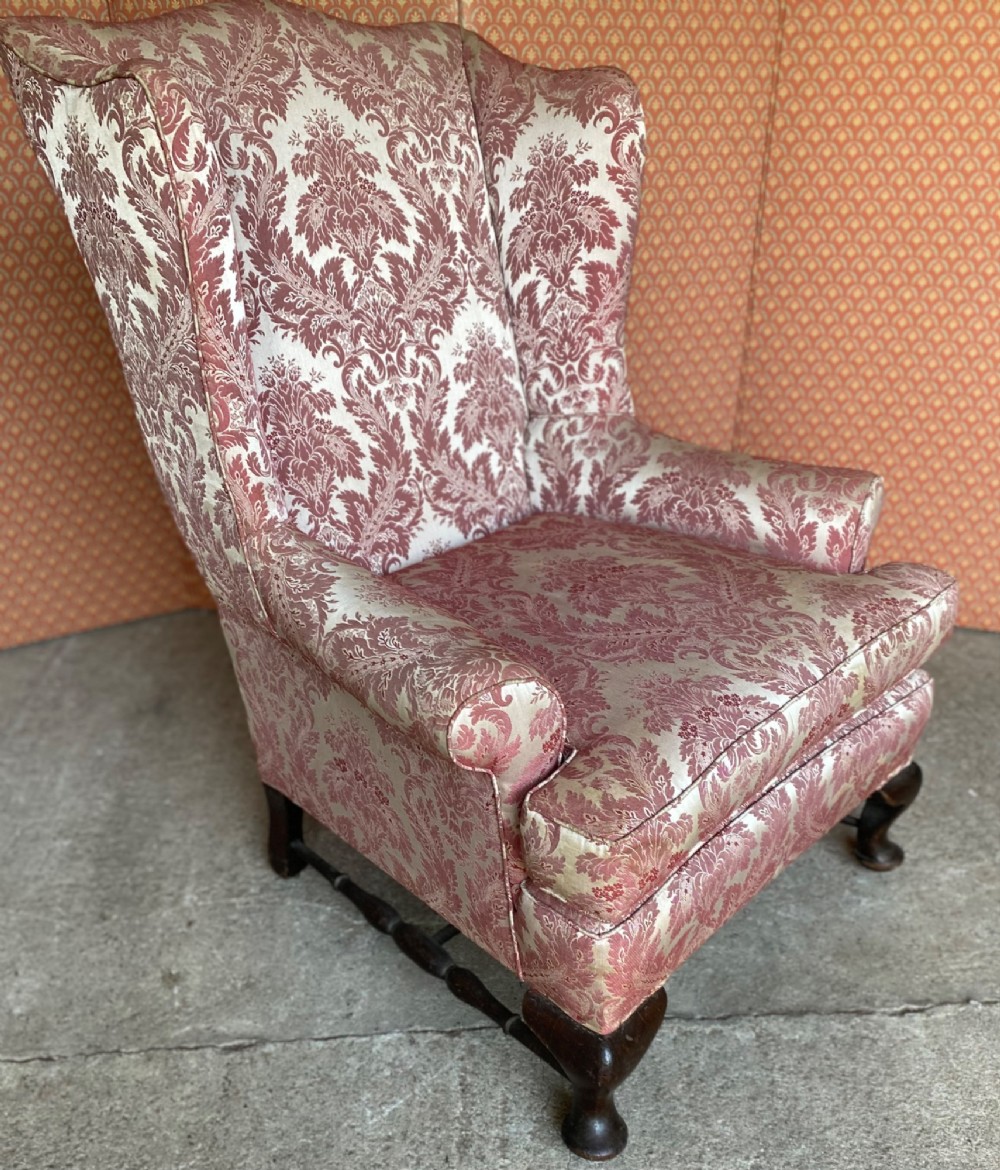 A high-back wingback armchair upholstered in rose pink and cream damask fabric, featuring rolled arms, a fitted seat cushion, and dark carved wooden legs. View III