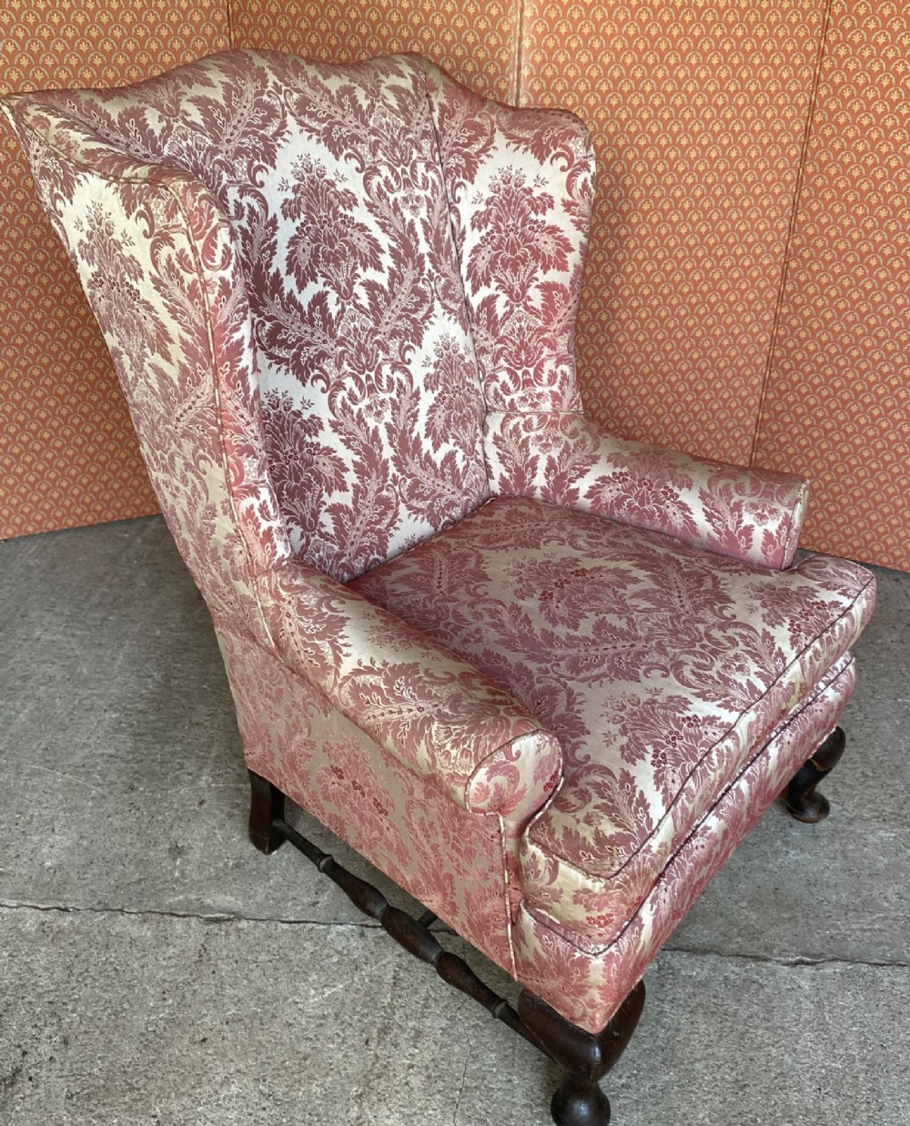 A high-back wingback armchair upholstered in rose pink and cream damask fabric, featuring rolled arms, a fitted seat cushion, and dark carved wooden legs. View IV