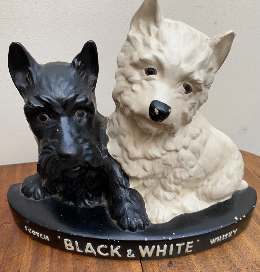 A vintage painted plaster advertising display figure featuring a black Scottish Terrier and a white West Highland White Terrier on a black base marked Scotch Black and White Whisky.