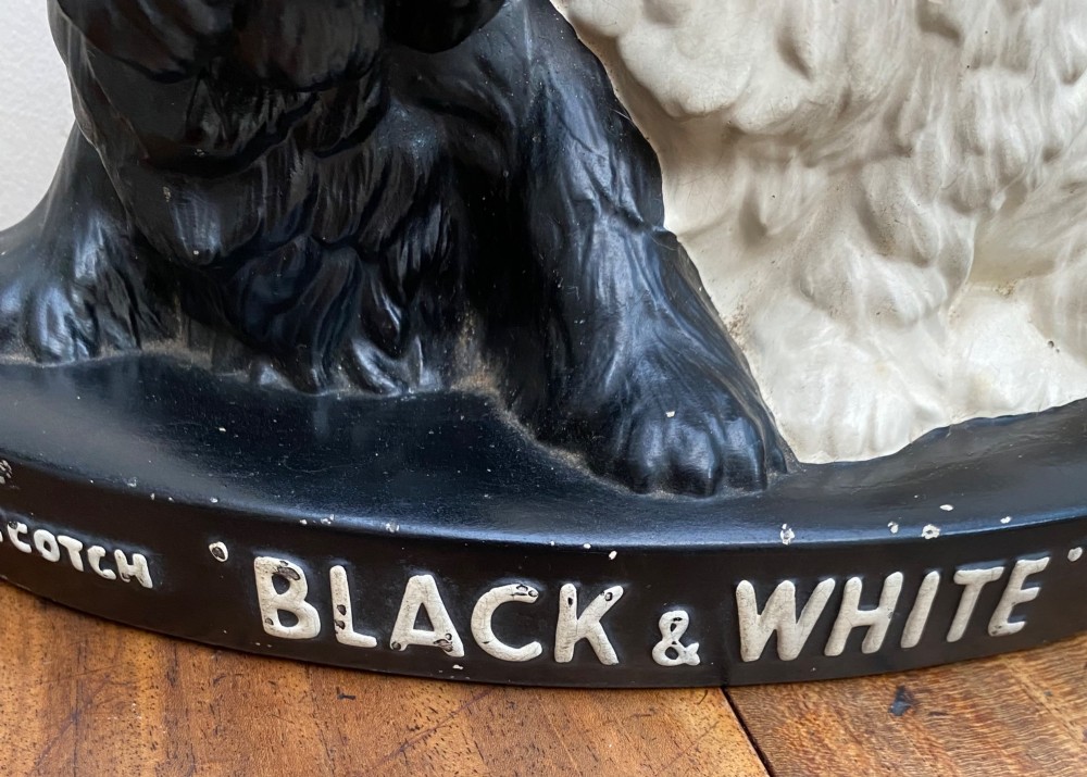 A vintage painted plaster advertising display figure featuring a black Scottish Terrier and a white West Highland White Terrier on a black base marked Scotch Black and White Whisky. View II