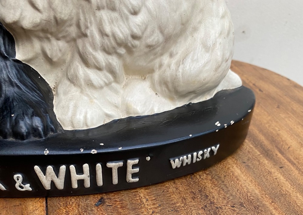 A vintage painted plaster advertising display figure featuring a black Scottish Terrier and a white West Highland White Terrier on a black base marked Scotch Black and White Whisky. View V