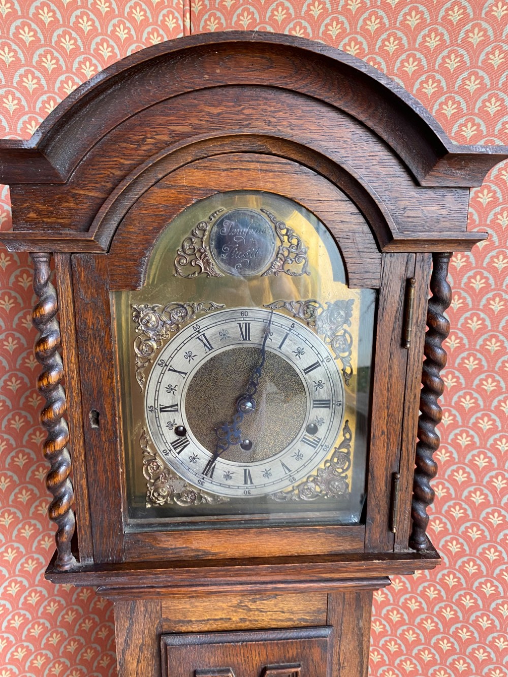 A Jacobean style oak grandmother clock featuring an arched top, barley twist columns, and a carved geometric panel door. View IV