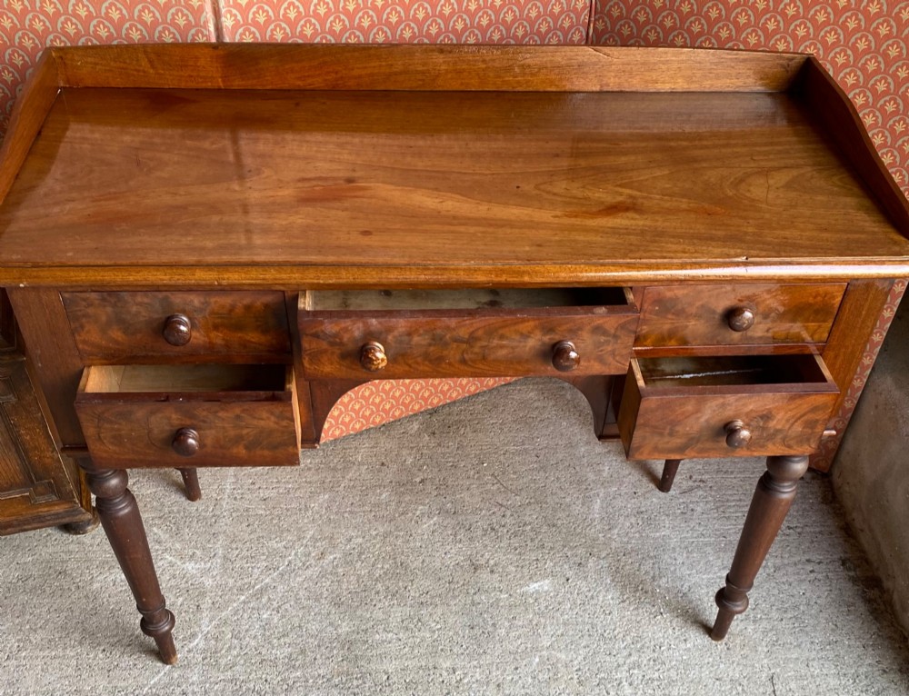 A Victorian mahogany writing desk featuring five drawers with turned knobs, turned legs, an arched kneehole, and a low gallery upstand. View III
