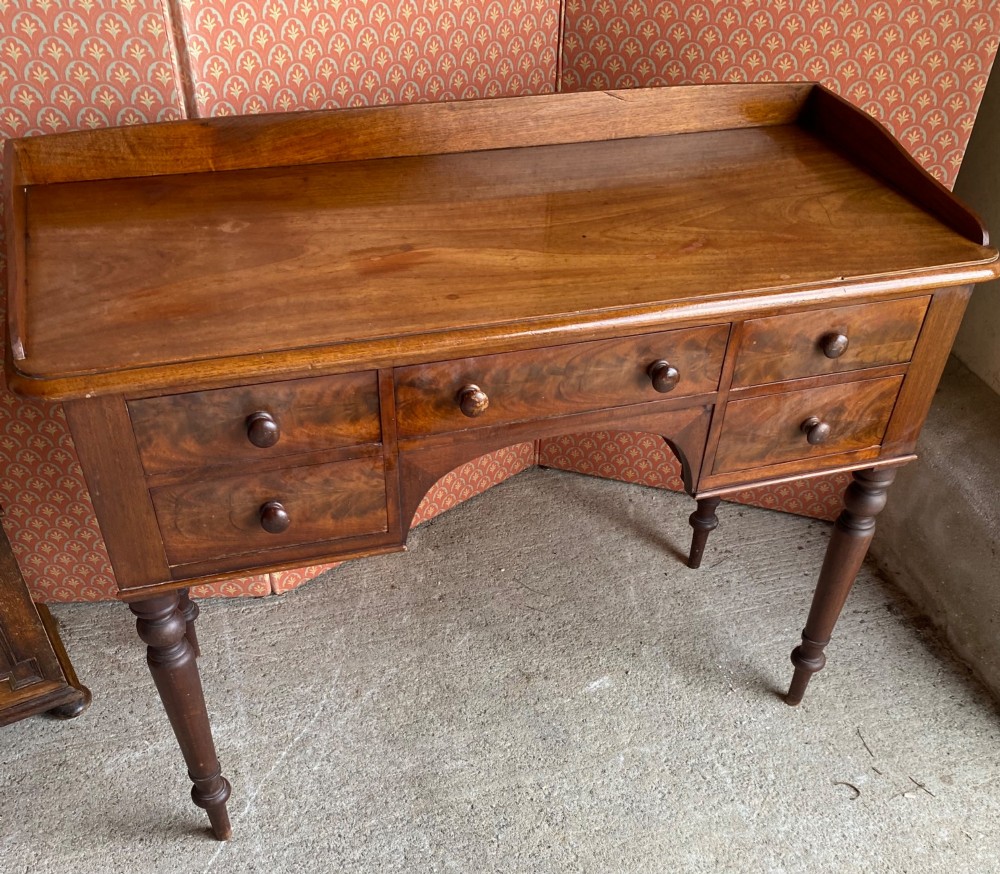 A Victorian mahogany writing desk featuring five drawers with turned knobs, turned legs, an arched kneehole, and a low gallery upstand. View IV