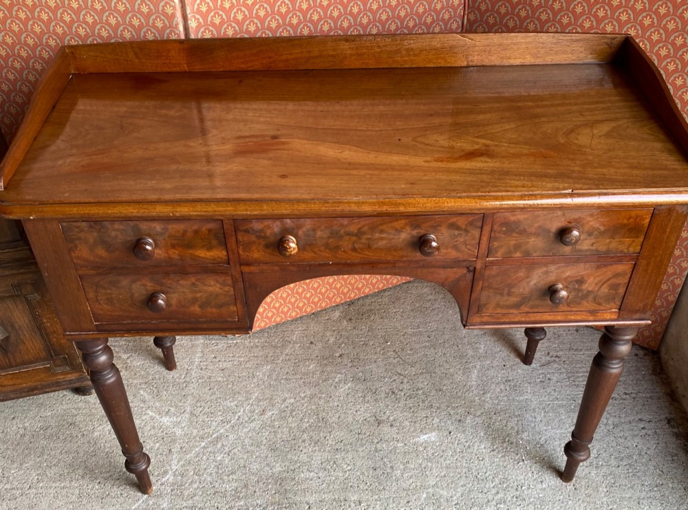 A Victorian mahogany writing desk featuring five drawers with turned knobs, turned legs, an arched kneehole, and a low gallery upstand. View V