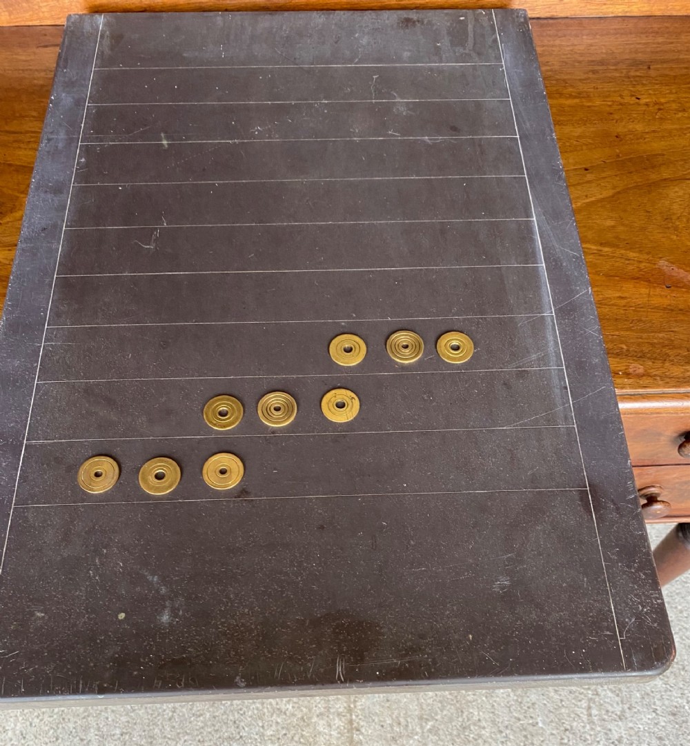 A rectangular dark grey slate shove hapenny board incised with horizontal scoring lines and several brass tokens. View III