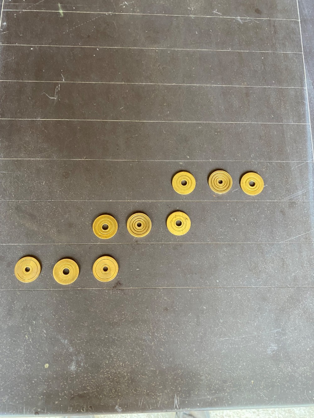 A rectangular dark grey slate shove hapenny board incised with horizontal scoring lines and several brass tokens. View IV