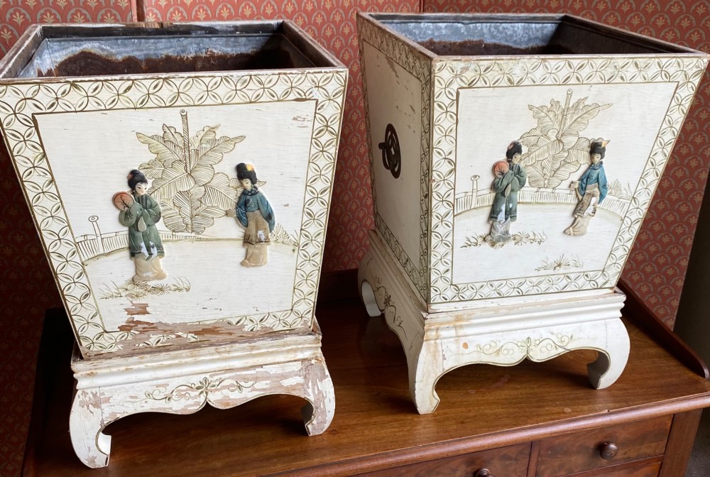 A pair of square cream painted wooden planters featuring raised figural motifs and banana palm tree designs on stepped bases with removable metal liners.