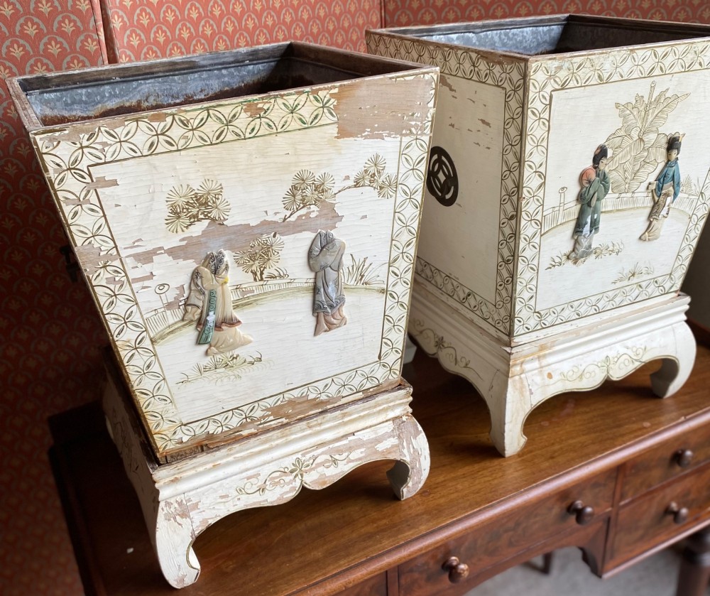 A pair of square cream painted wooden planters featuring raised figural motifs and banana palm tree designs on stepped bases with removable metal liners. View V
